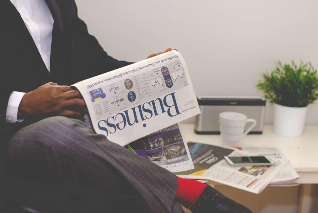 Man reading a business newspaper with a cup of coffee and smartphone on the table