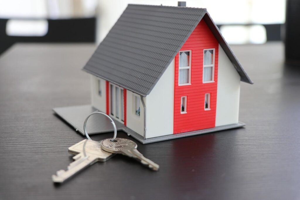 A tiny red and white miniature house placed alongside a set of keys