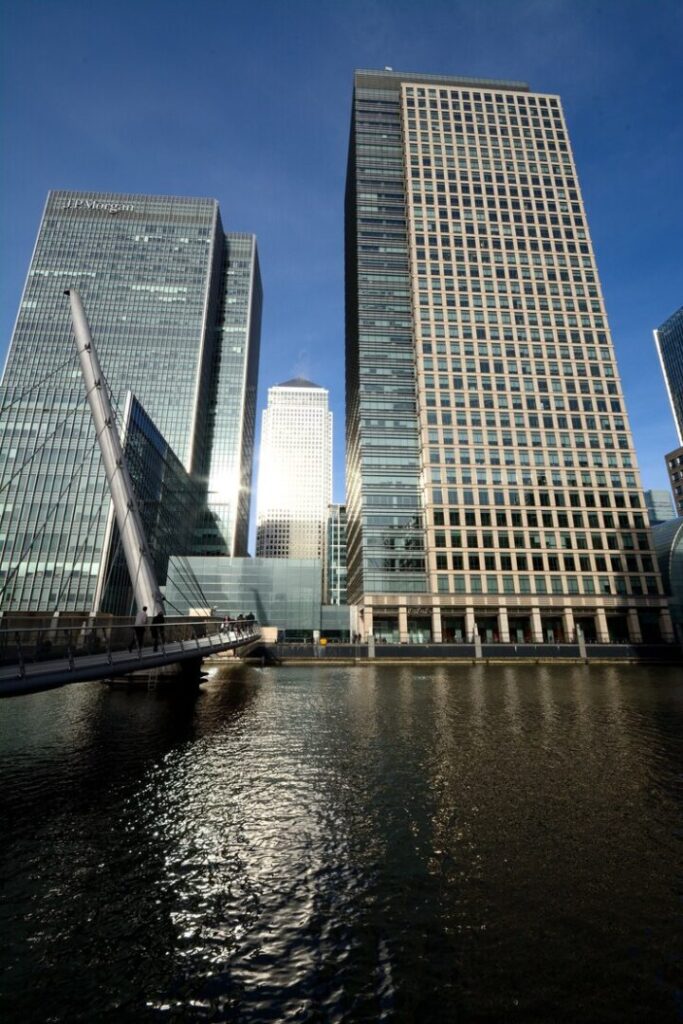 vertical-shot-tall-wedge-buildings-near-bridge-water-sunny-day