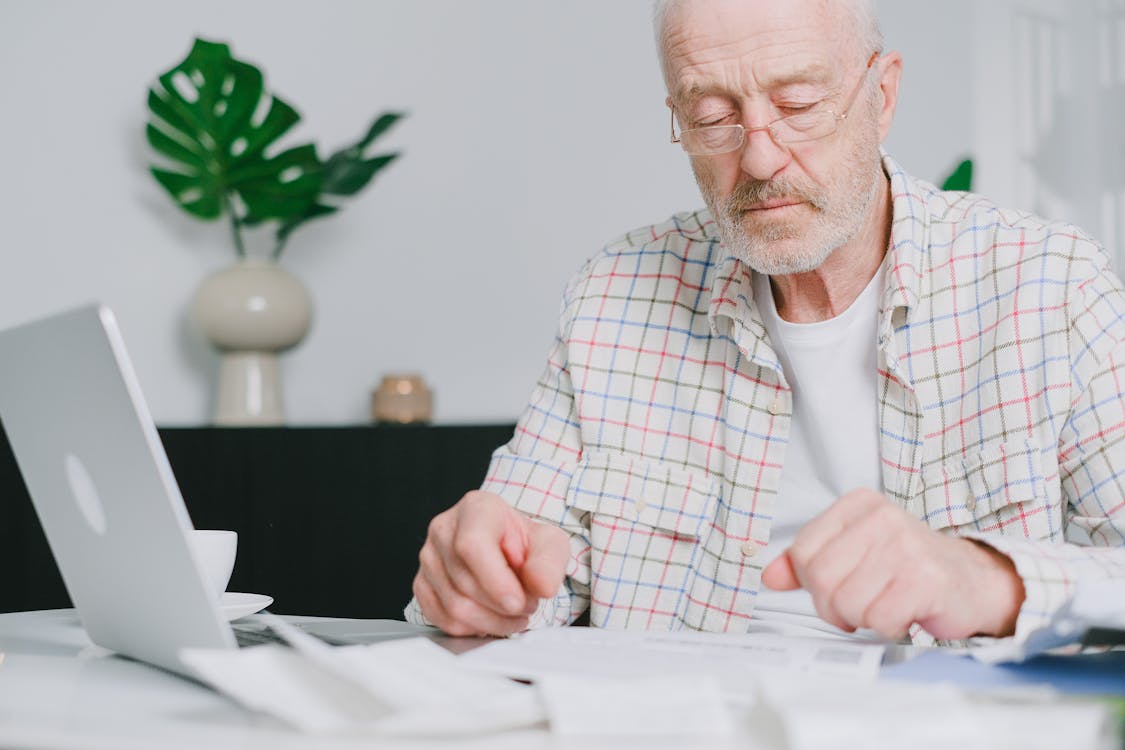 An elderly man thoughtfully looking at a table, symbolizing deep consideration and evaluation of construction plans.