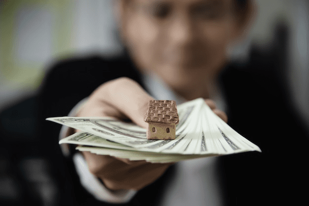 An image of a man holding banknotes with a miniature home on it 