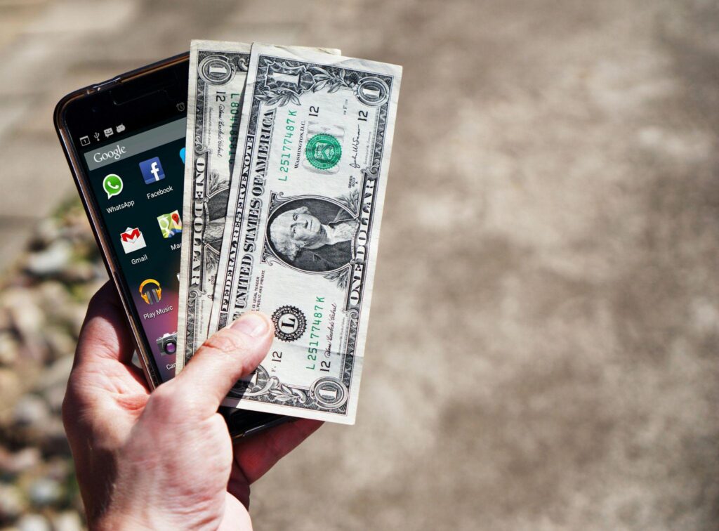 A person holds one-dollar bills and a phone