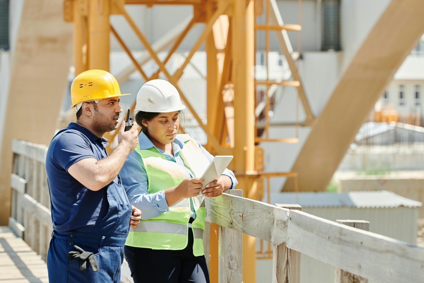 A Man in a Blue Shirt Using a walkie-talkie while Standing Beside the Woman Near the Wooden Fence