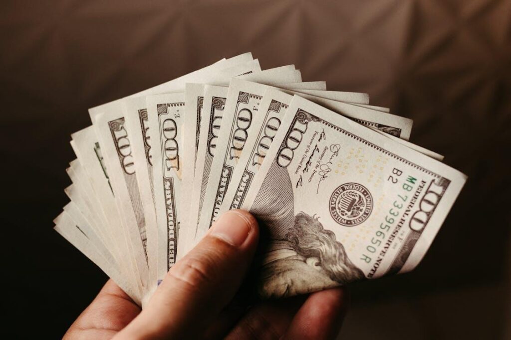A hand holding 100-US dollar banknotes