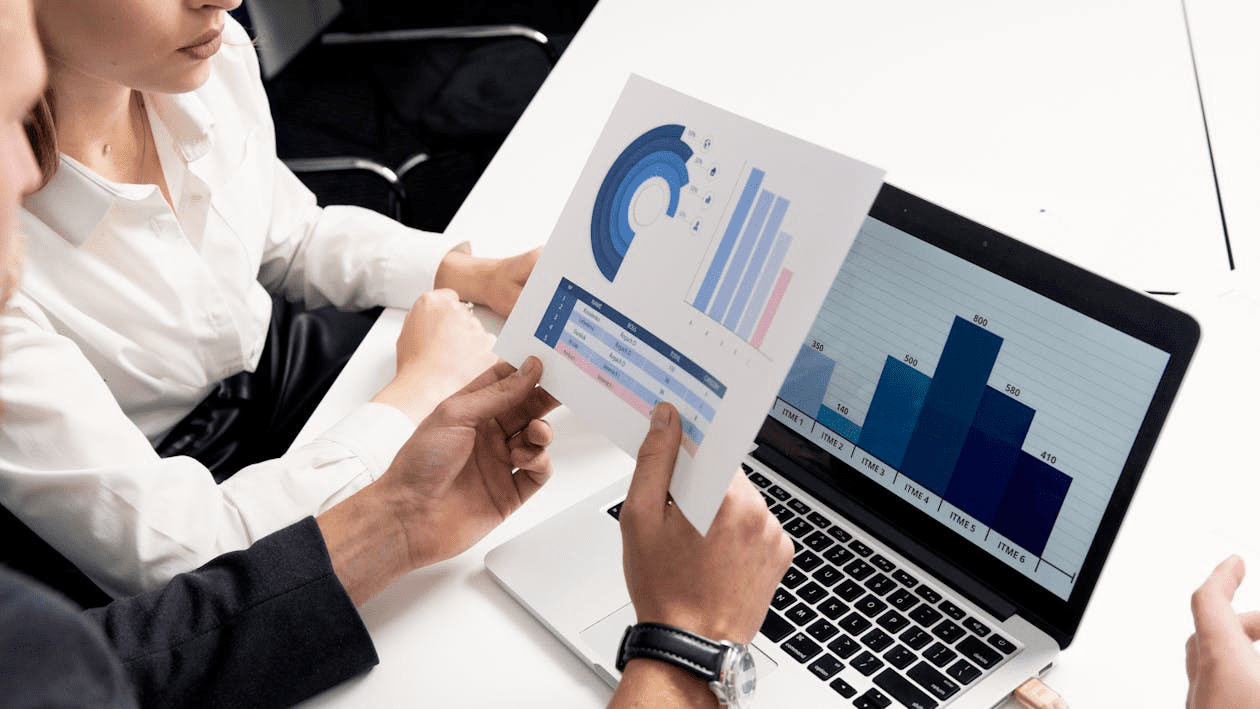Two people looking at graphs on laptop and papers