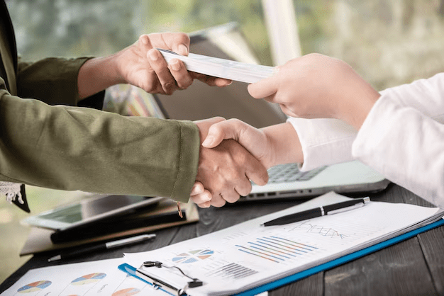 Two people shaking hands and exchanging a document
