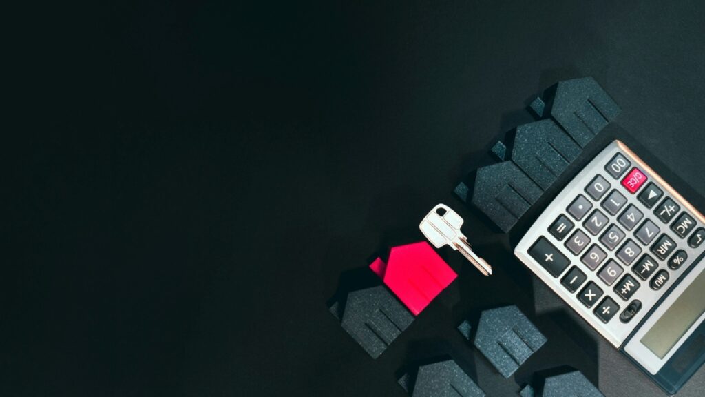 cut-outs of houses and a key lined against a calculator on a black background