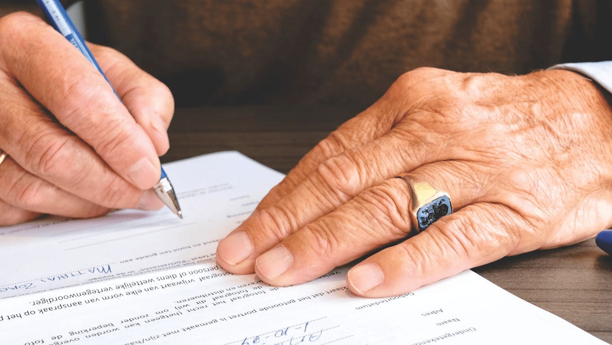 a person's hands signing a document with a pen.