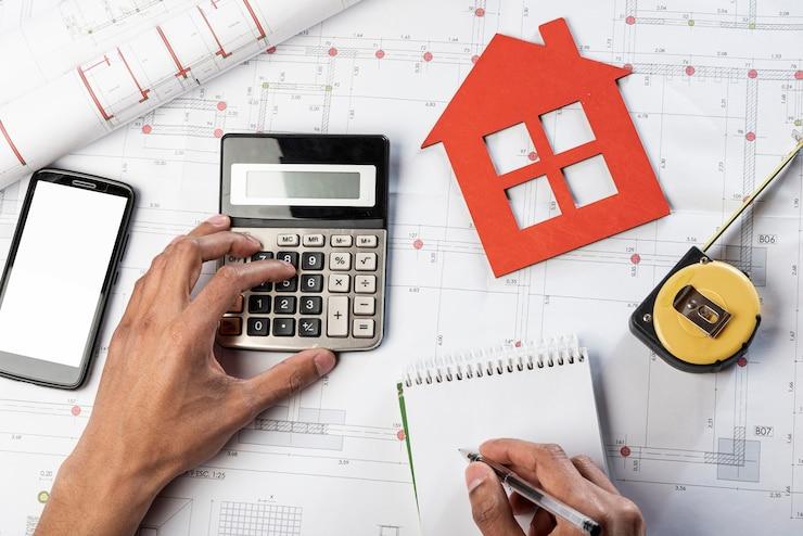 A person using a calculator, writing in a notepad, on construction blueprints