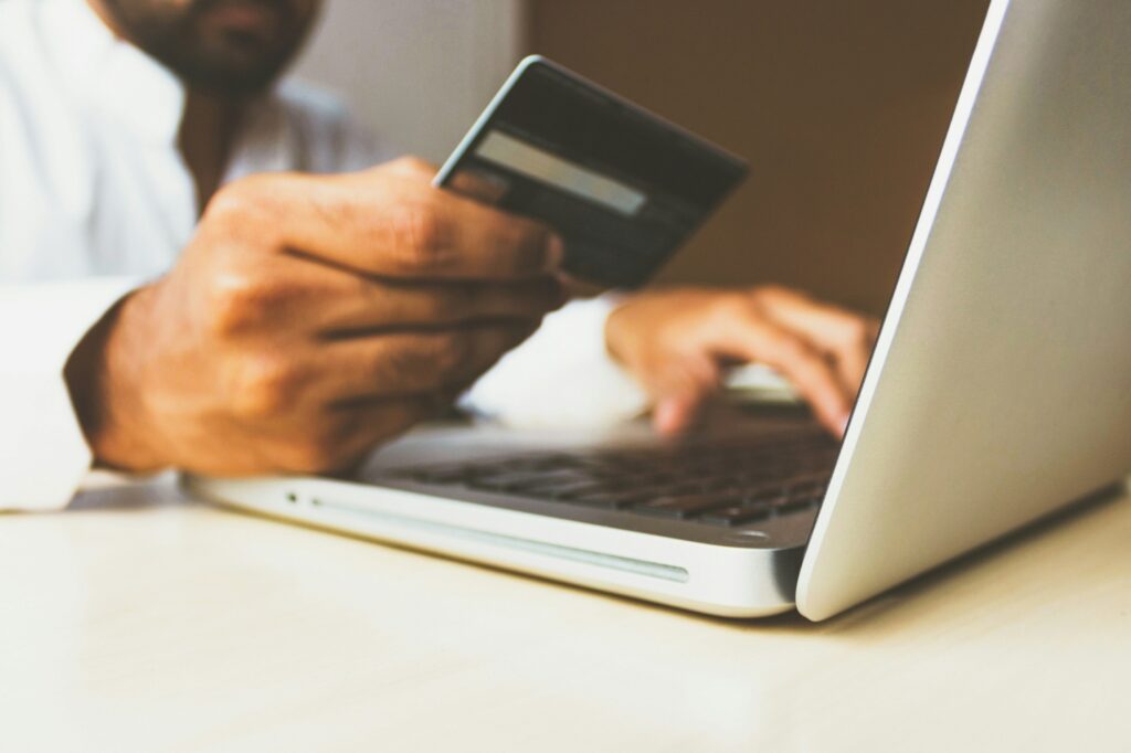 close-up of a man holding a credit card above an open laptop 