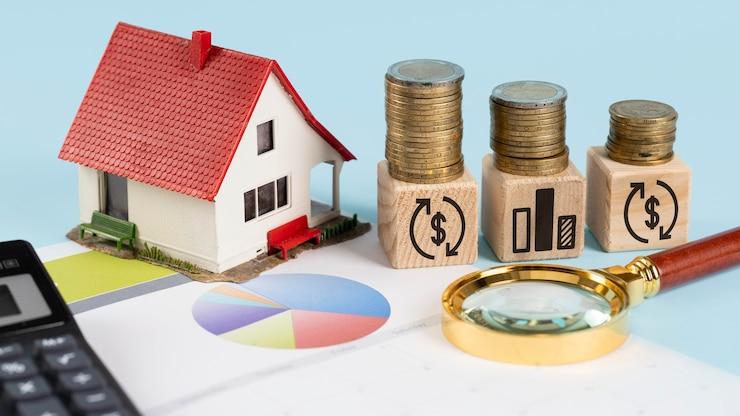 A miniature home next to wooden blocks with stacks of coins