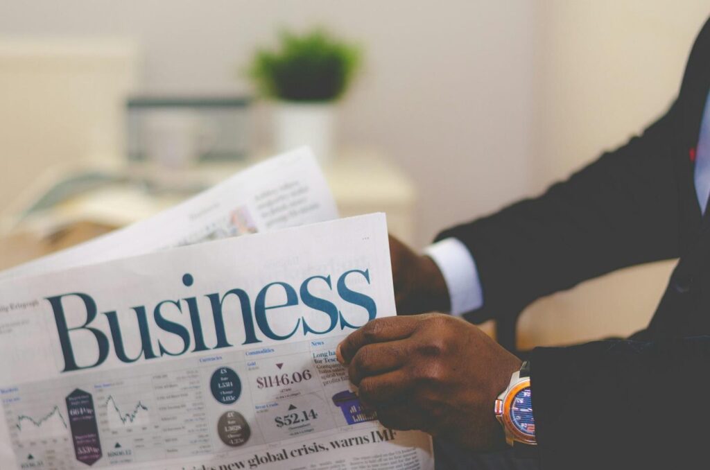 An image of a man opening a newspaper with a headline spelling out ‘business’.