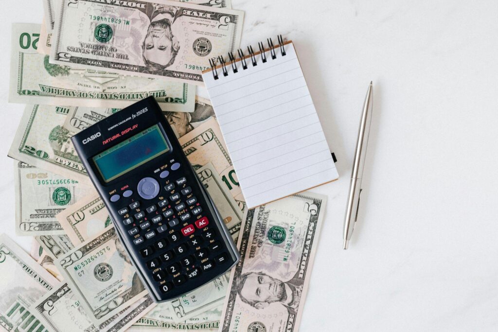 Calculator, stack of cash, and pen on a desk