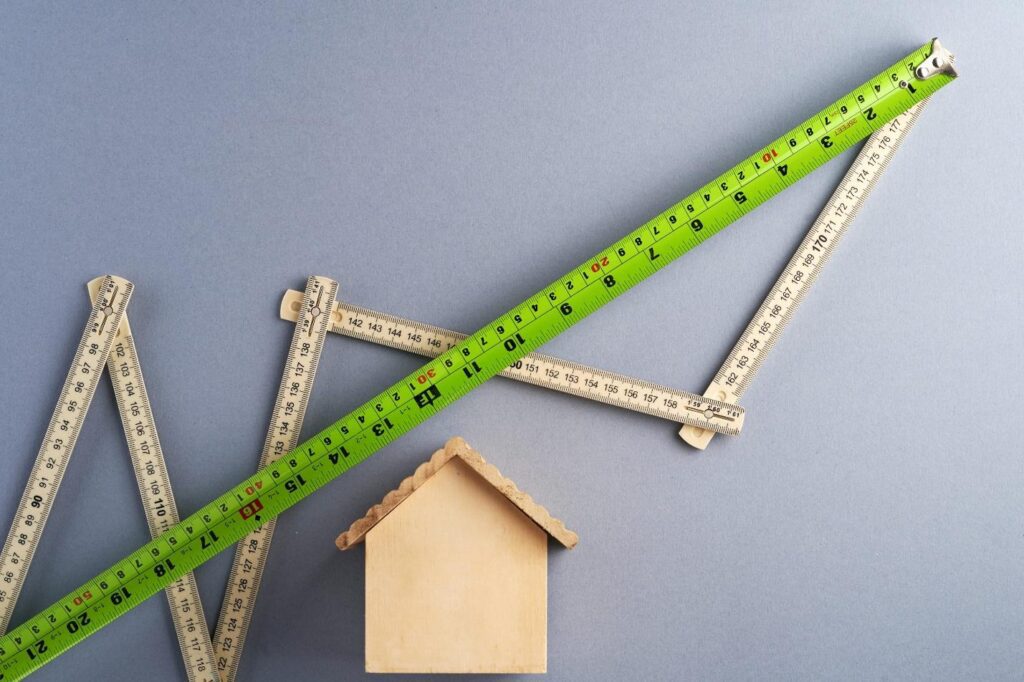 An image of a wooden, miniature house with two measuring tapes making graph-like lines.