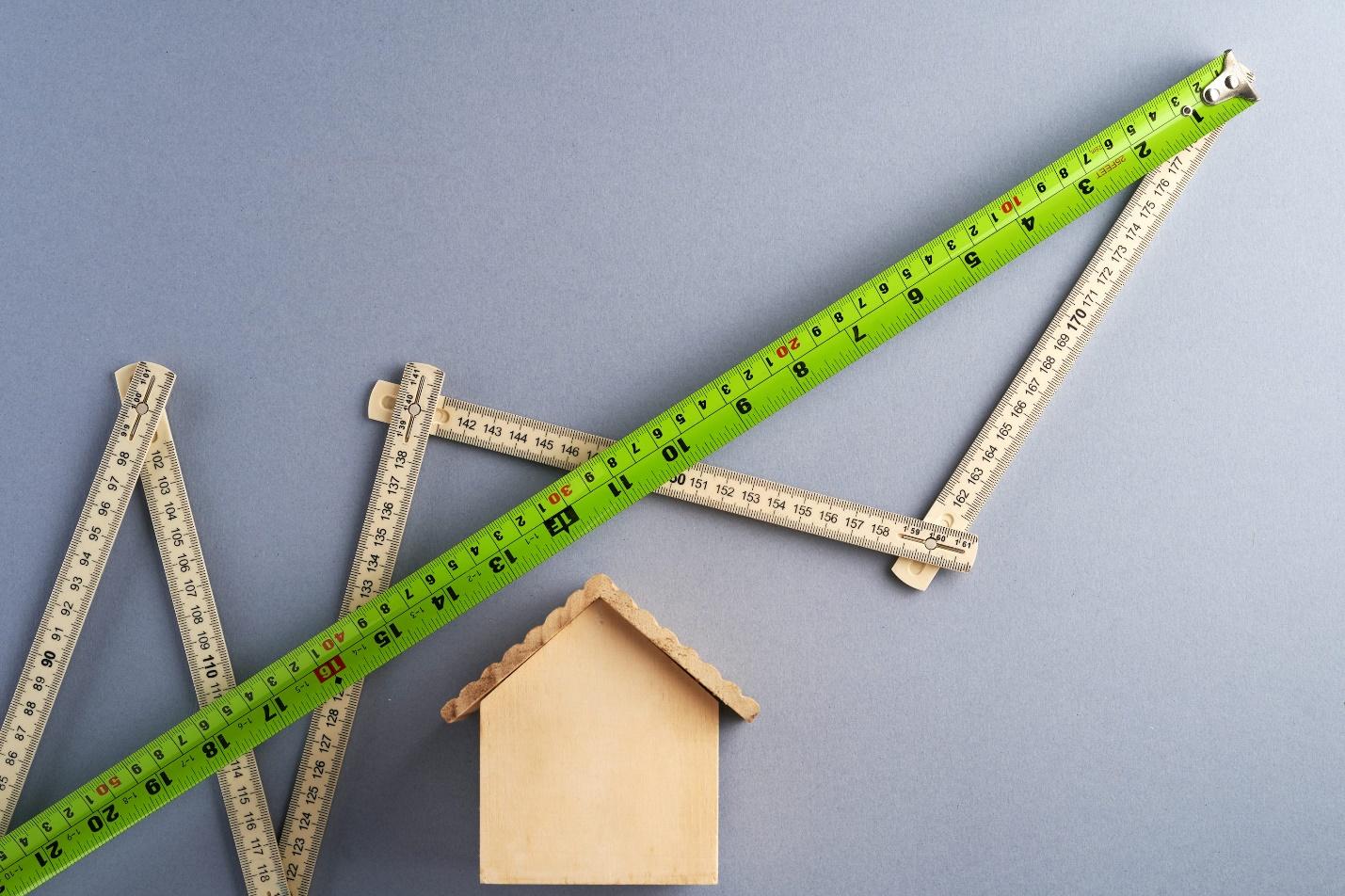 An image of a wooden, miniature house with two measuring tapes making graph-like lines.