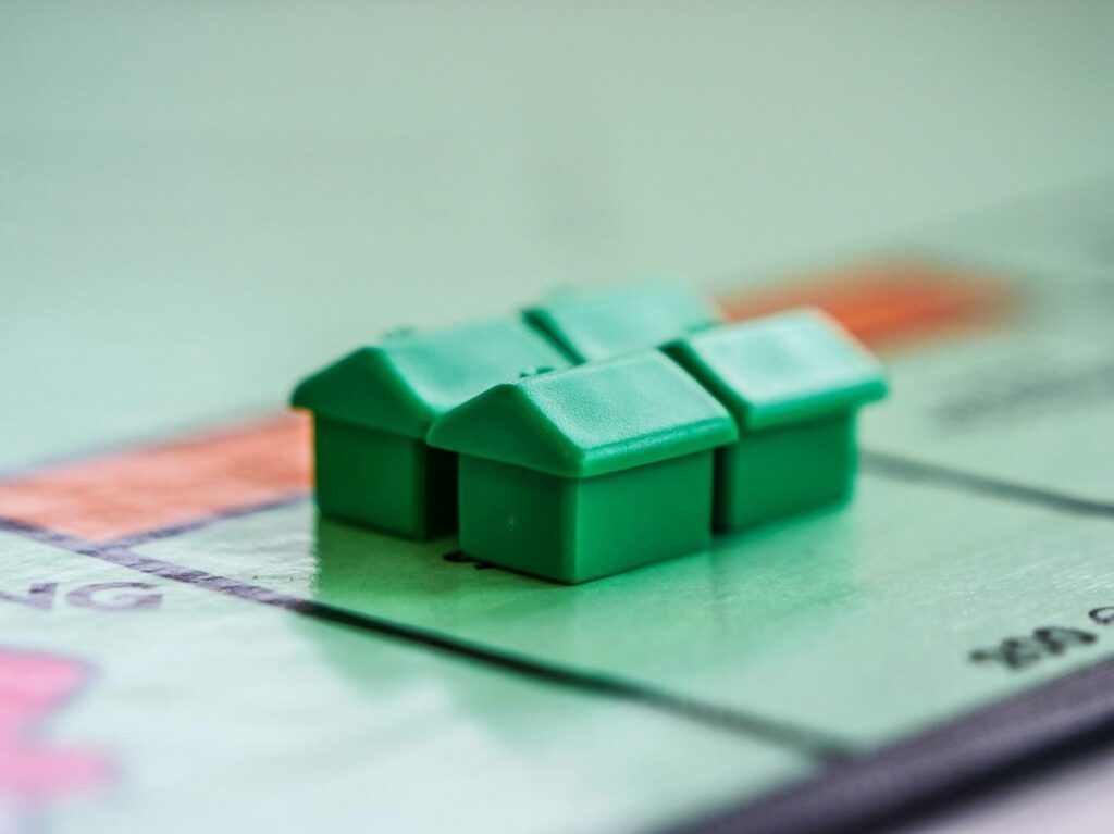 An image of four miniature Monopoly houses set on the Monopoly board