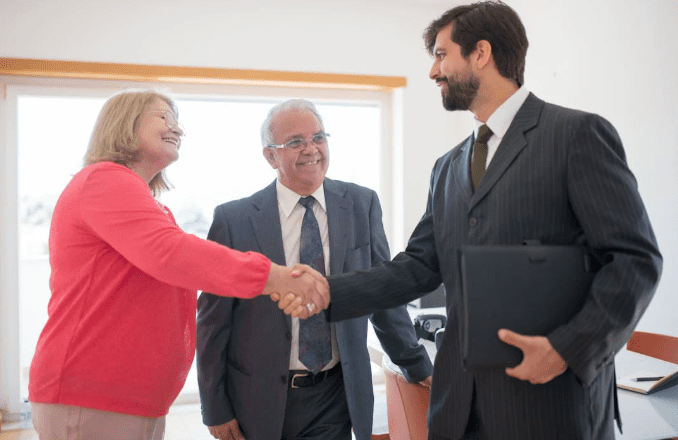 A man and a woman shaking hands across a table, symbolizing a business agreement