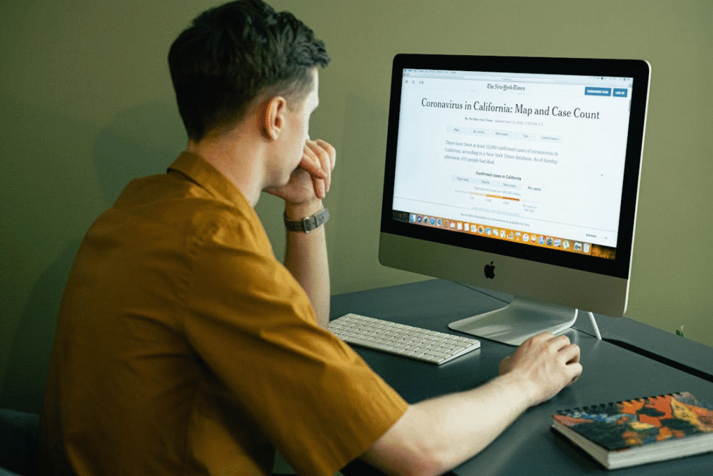 A man in a brown shirt looking at a desktop screen displaying COVID-19 case data for California.