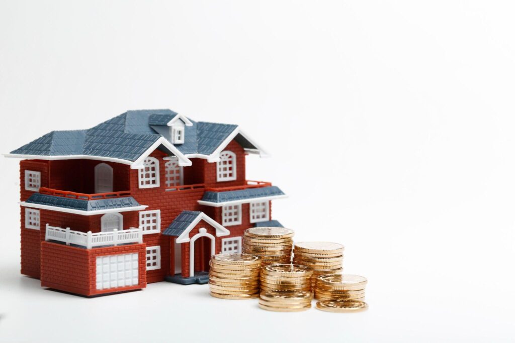 Miniature red-roof house next to stacked coins 