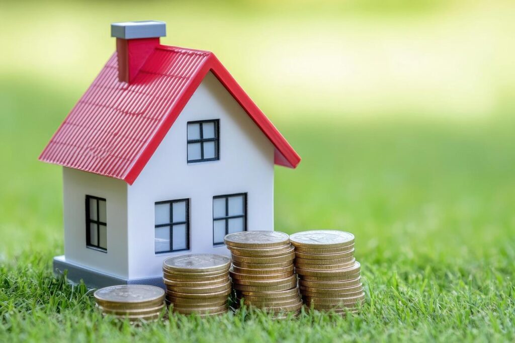 A model house can be seen on the grass with coins in front of it