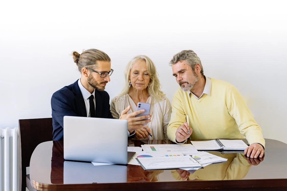 A young male financial advisor shows something on his phone to an older couple