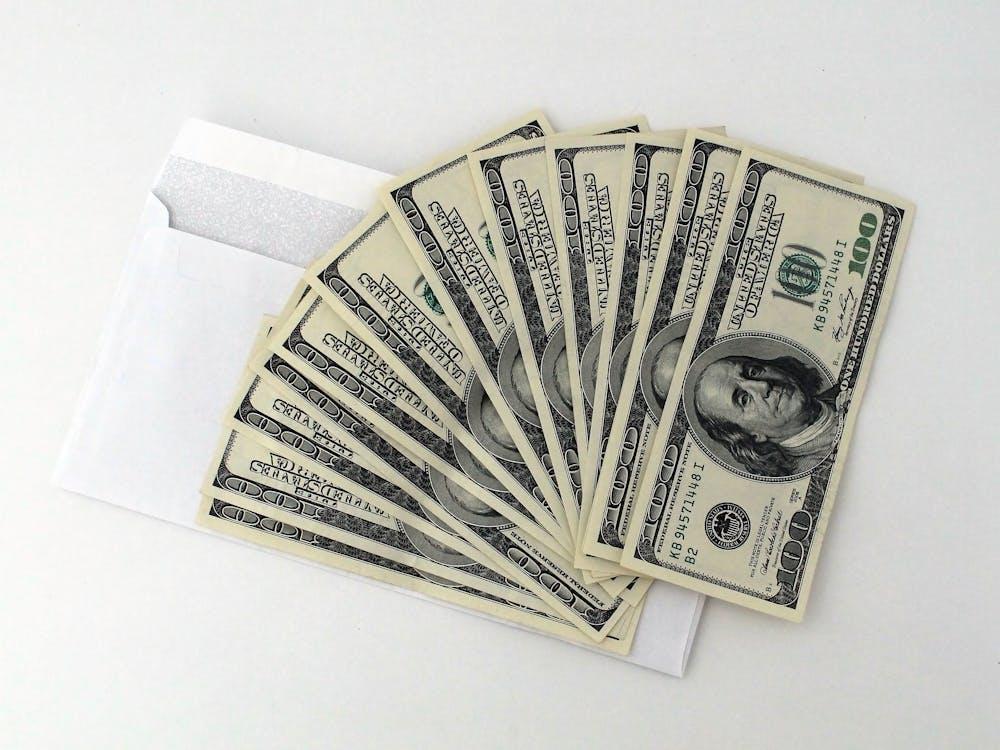 A white envelope holds a fanned stack of U.S. hundred-dollar bills.