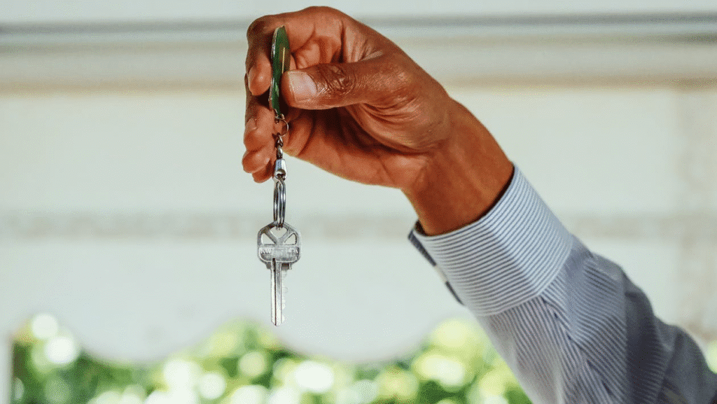A person in a blue dress shirt holding a single house key with a green keychain.