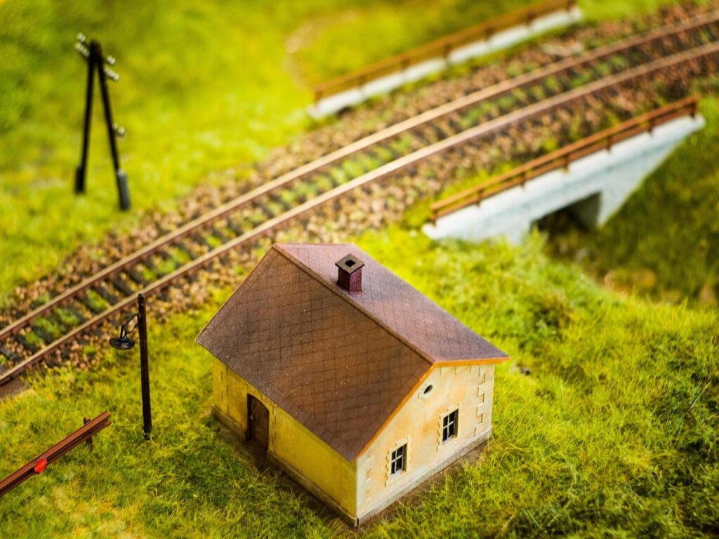 An old model house can be seen with a train track beside it in a grassy area