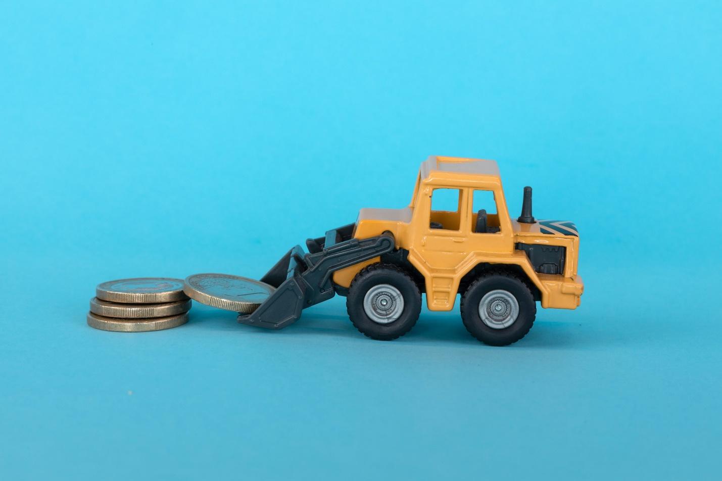 An image of a toy truck excavator picking up on coins in a blue background.