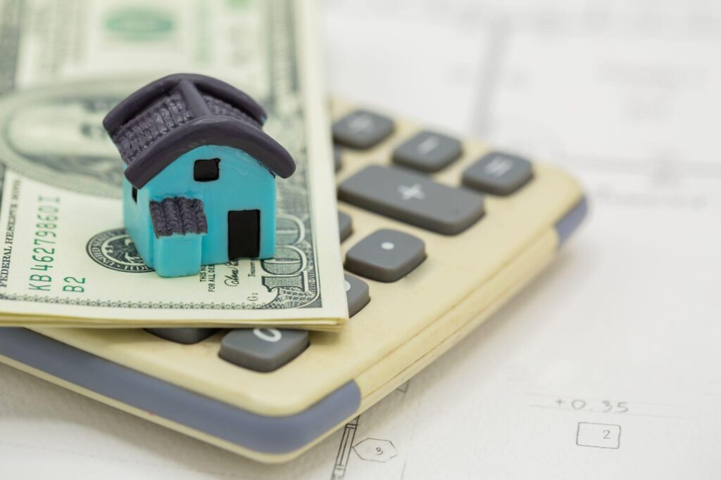 Miniature house sitting on dollar bills atop a calculator