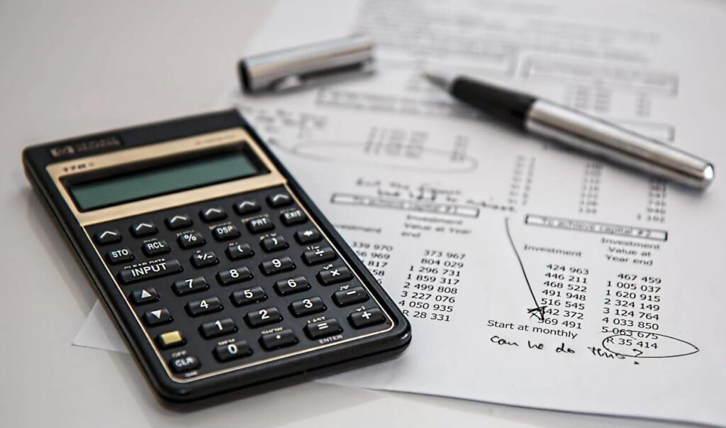 A picture of a calculator, spreadsheet and a pen placed on a white table