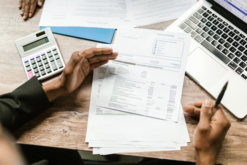 An image of a person’s hands, bank related documents, a calculator, and a laptop