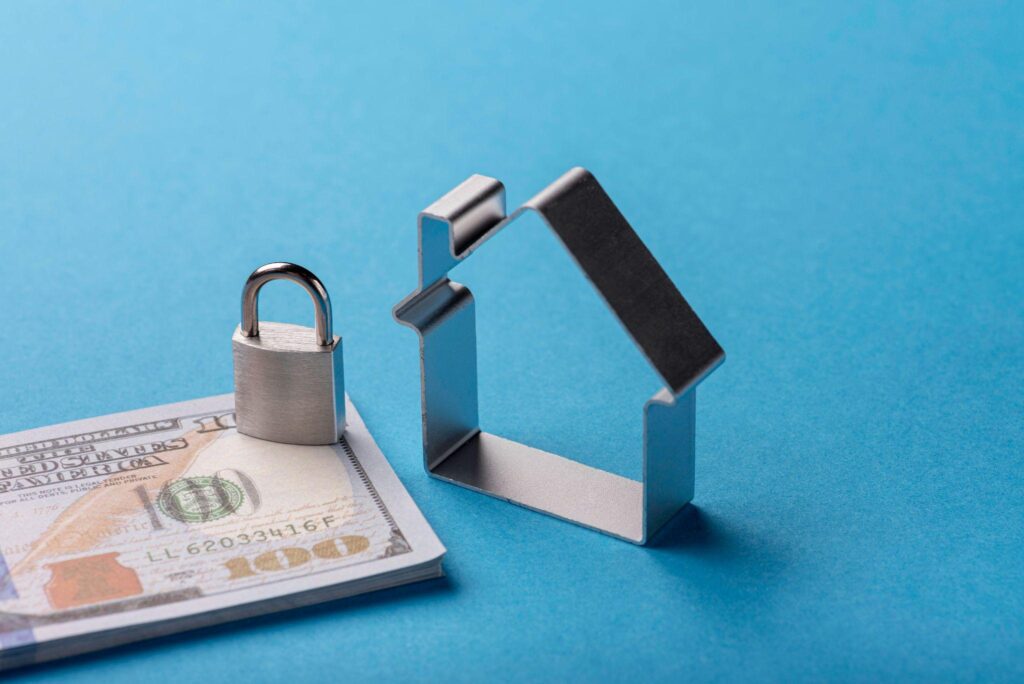 Metal house outline and padlock resting on U.S. currency against a blue background