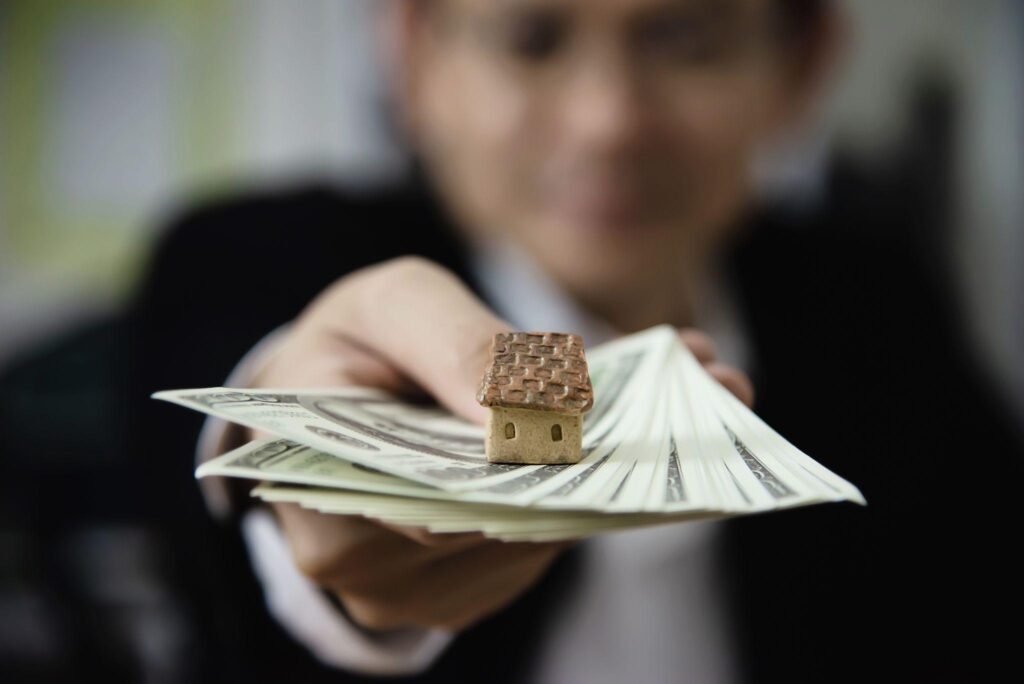 Businessperson handing over a stack of money with a small house model on top