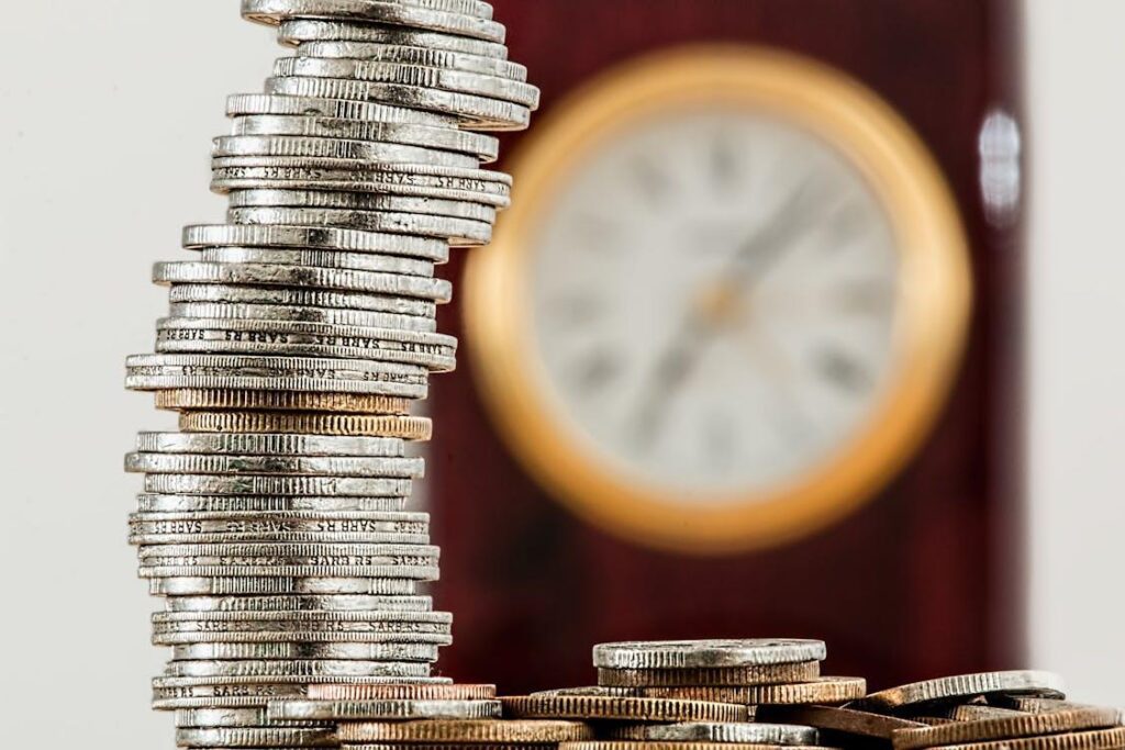 An image focused on a pile of coins with a blurred out clock in the background