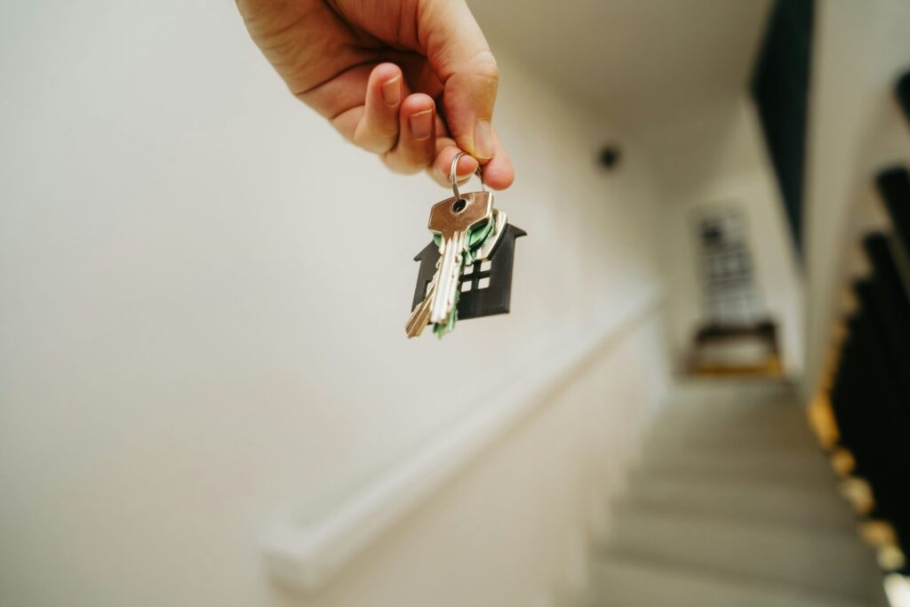 A set of house keys dangled by a person with blurry staircase in the background