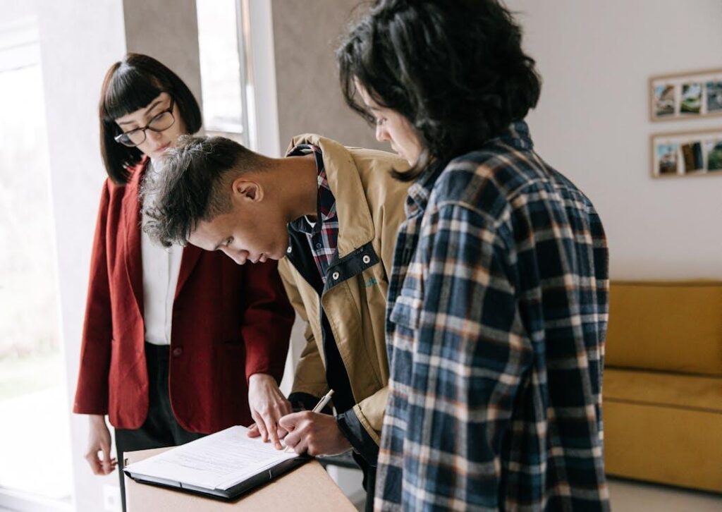 An image a man signing documents with two women standing beside him