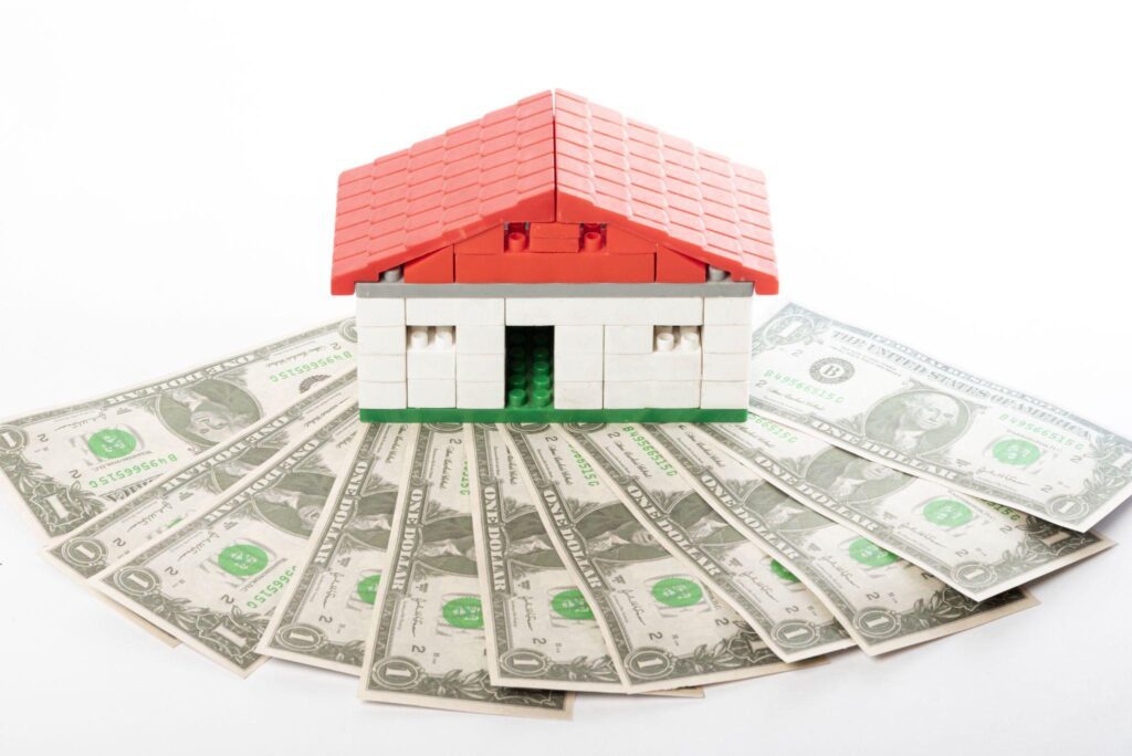 Red-roof toy house surrounded by U.S. dollar bills in a circular layout