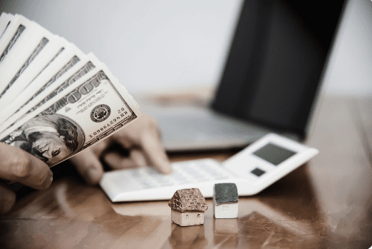 an individual holding cash while typing on a calculator