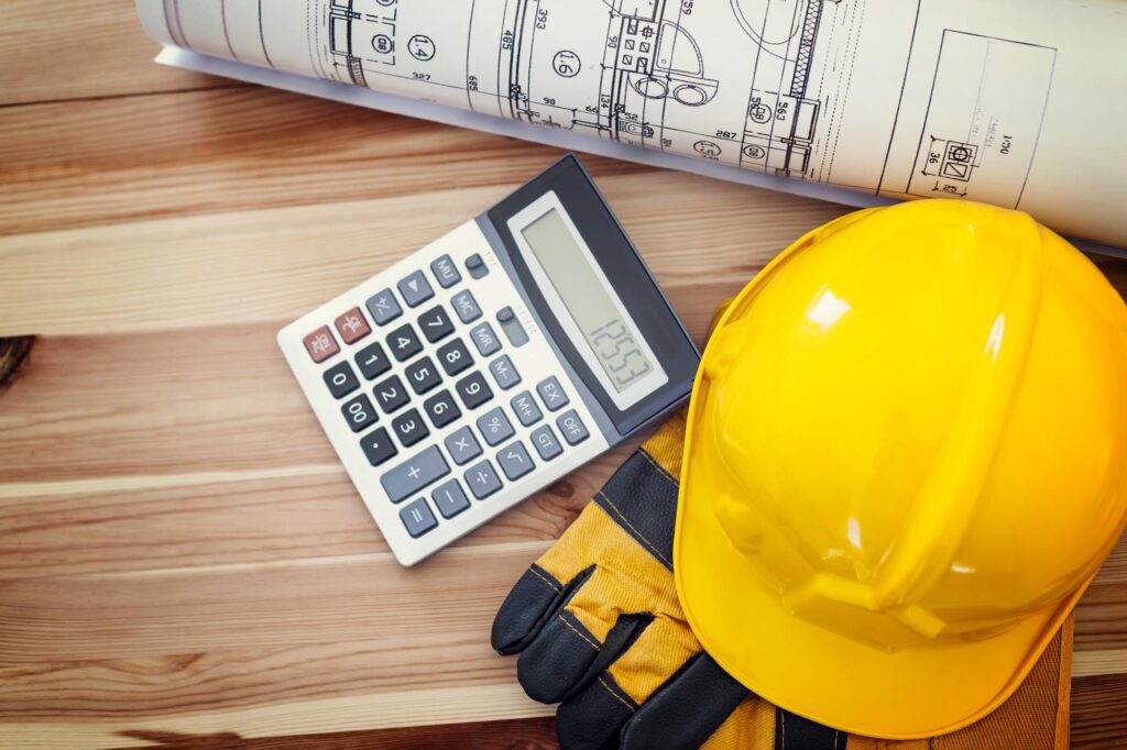 Yellow hard hat, building plans, and calculator on a wooden table