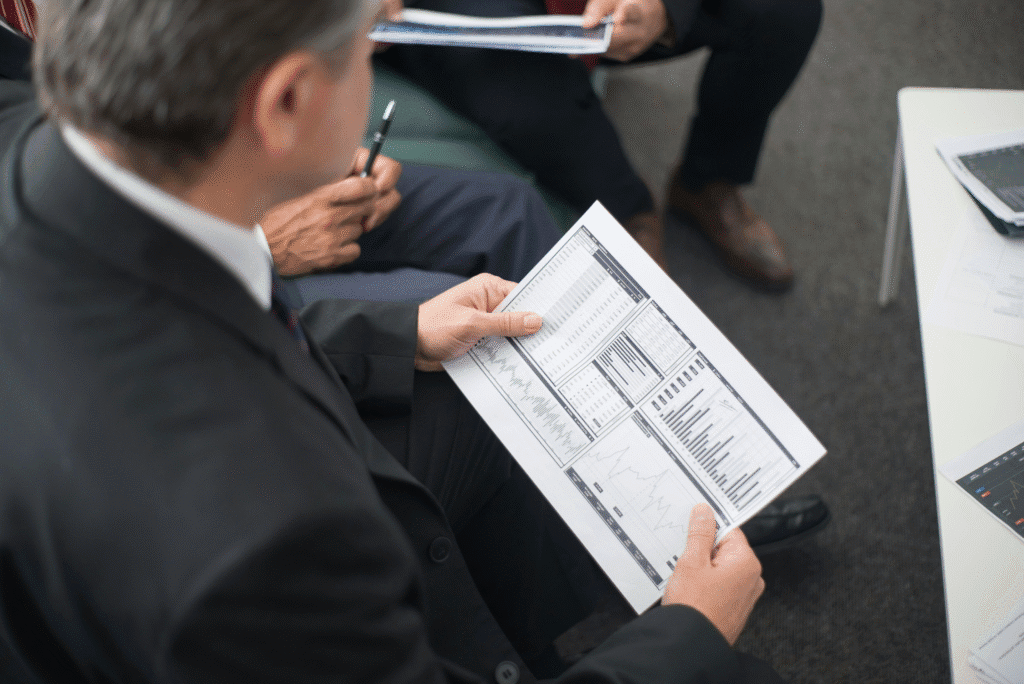a man sitting in a meeting with other people holding a document with graphs