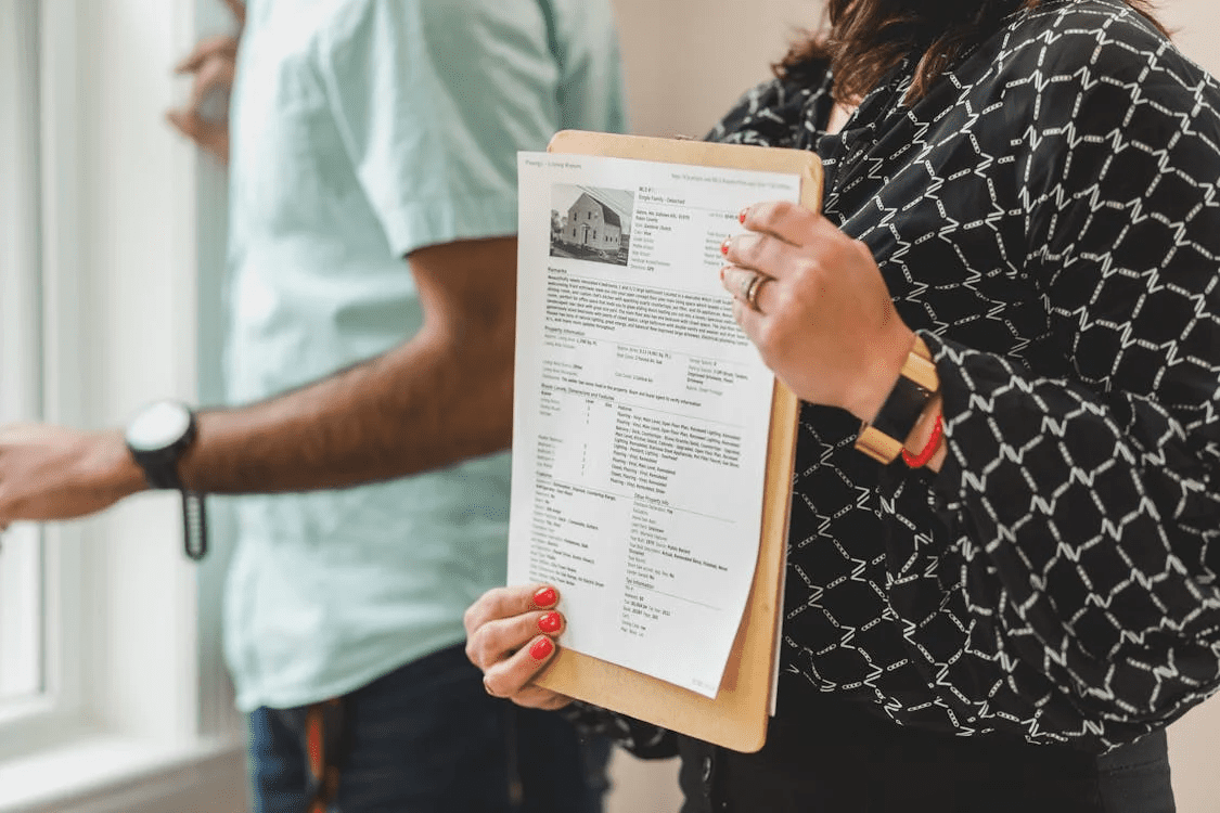 a woman holding a clipboard with a rental property paper on it, standing next to a man by the window