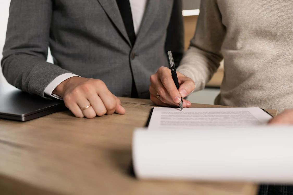 two men standing next to each other, signing a form placed on a wooden table