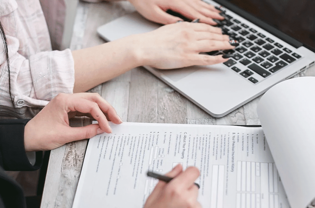 An image of two people, one using a laptop, the other with a document, possibly discussing an agreement.