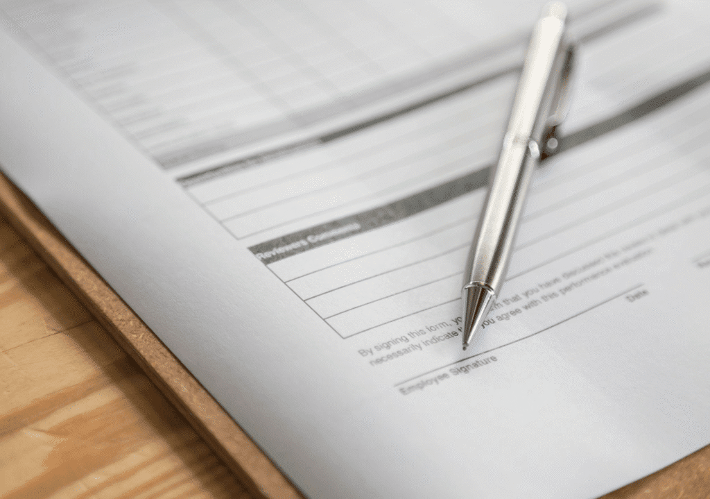 an empty form on a clipboard placed on a desk with a silver pen on it