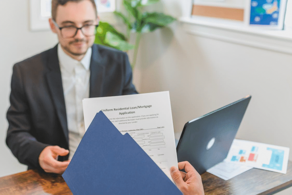 a person taking out residential loan forms from a folder sitting across another person at the table