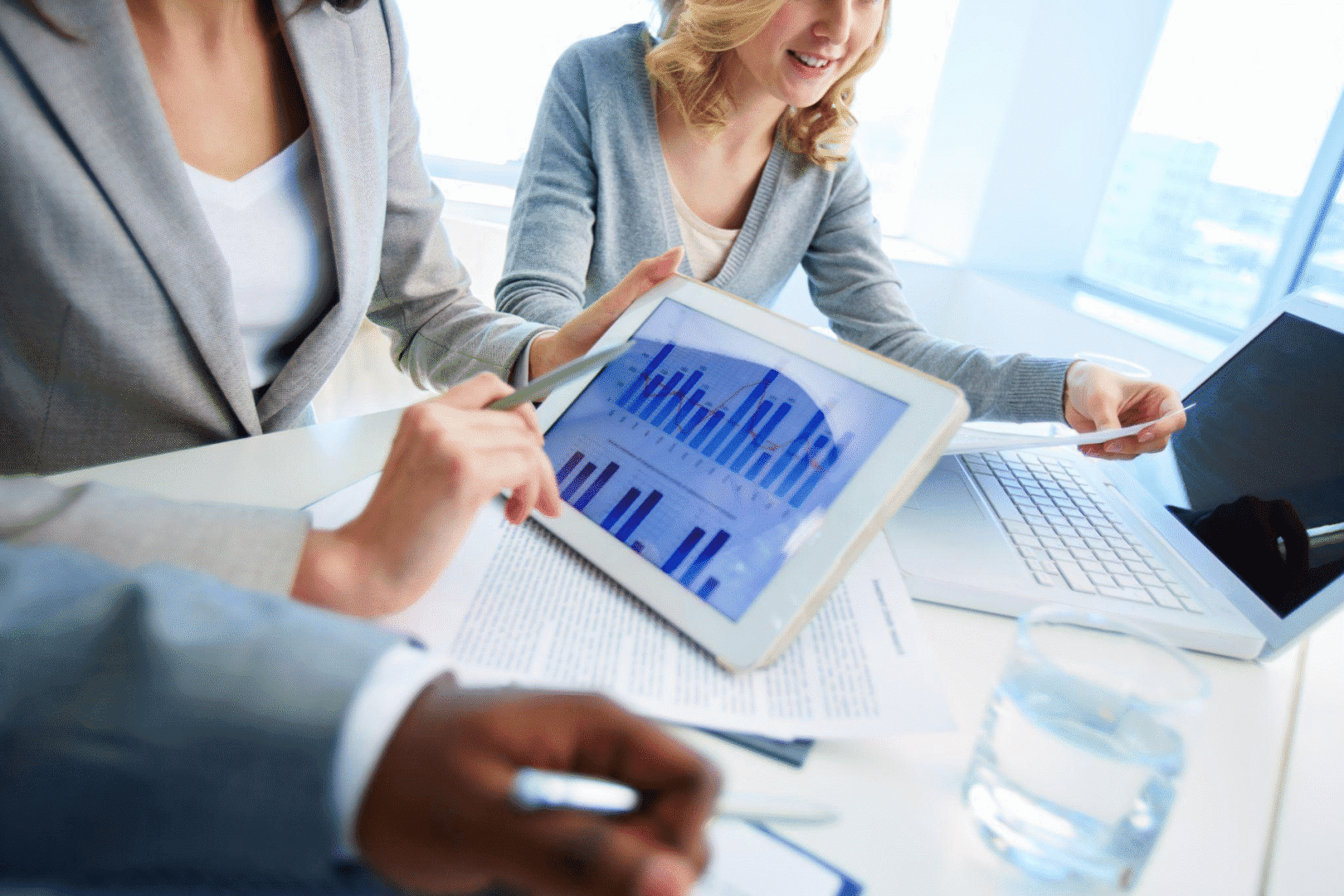 people sitting at a desk next to each other and going through graphs on screens and documents