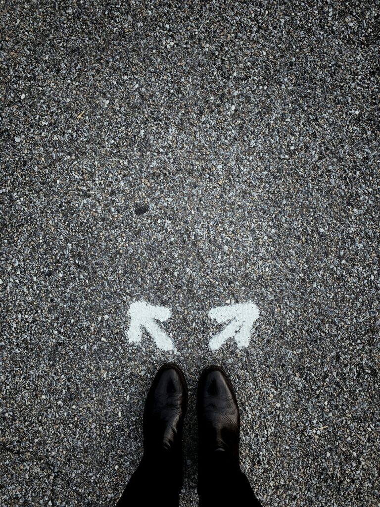A person standing at the center of a road with two arrows painted on it in white, pointing in two different directions