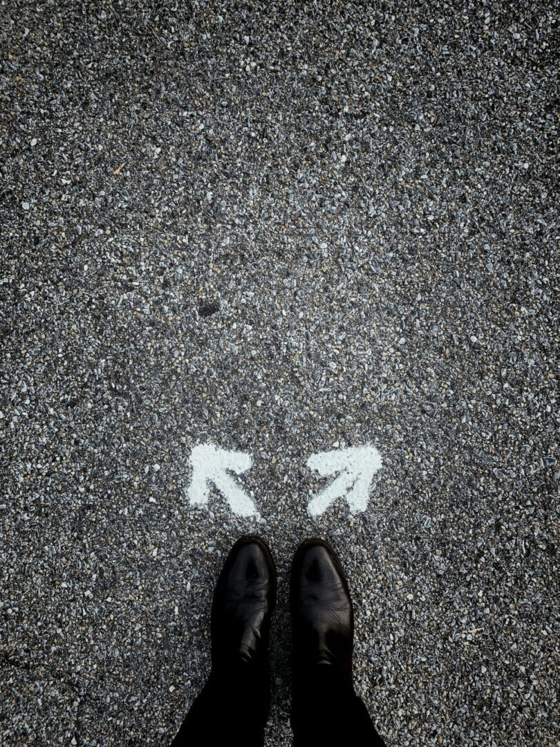 A person standing at the center of a road with two arrows painted on it in white, pointing in two different directions