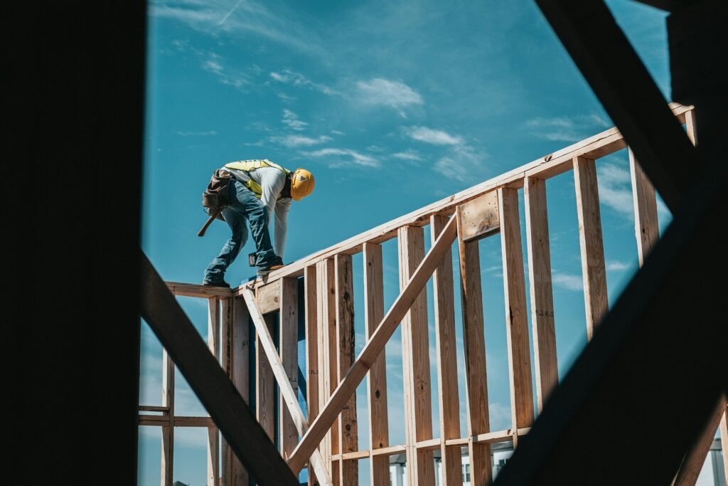 A man in a yellow hard hat fixing a wooden construction beam